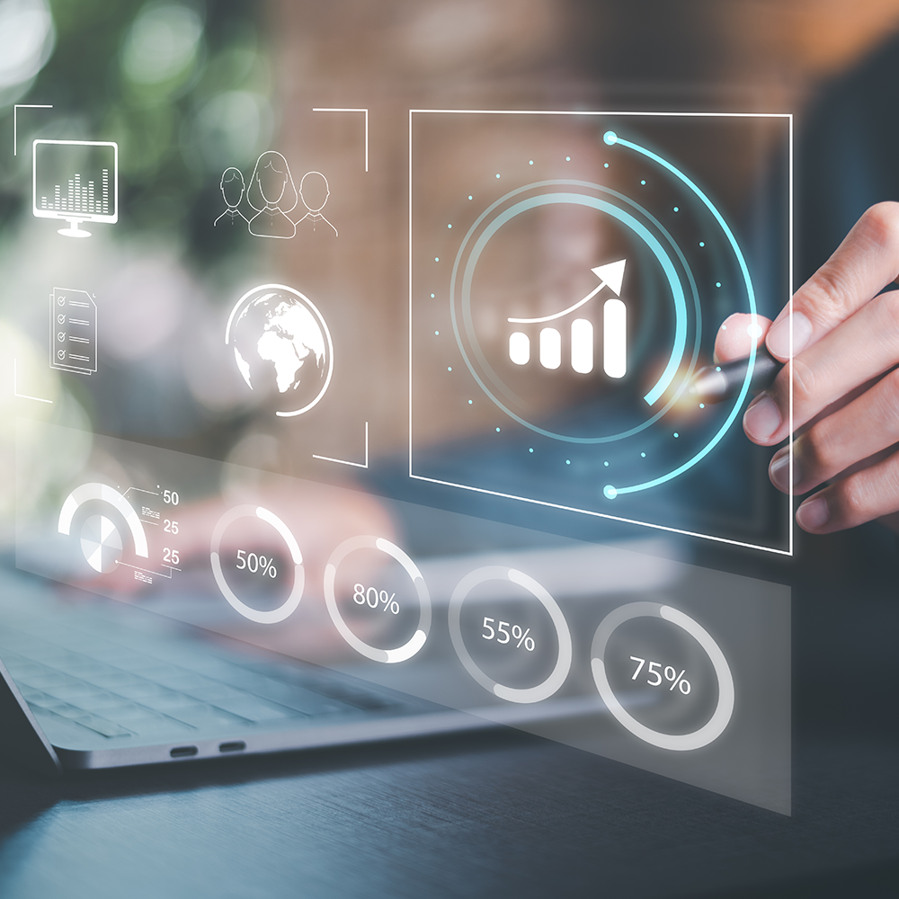 A person interacting with a transparent digital interface displaying data analytics icons, including a rising bar chart, global network, and user group symbols. Circular progress indicators show percentages ranging from 50% to 80%, overlaid above a laptop keyboard.